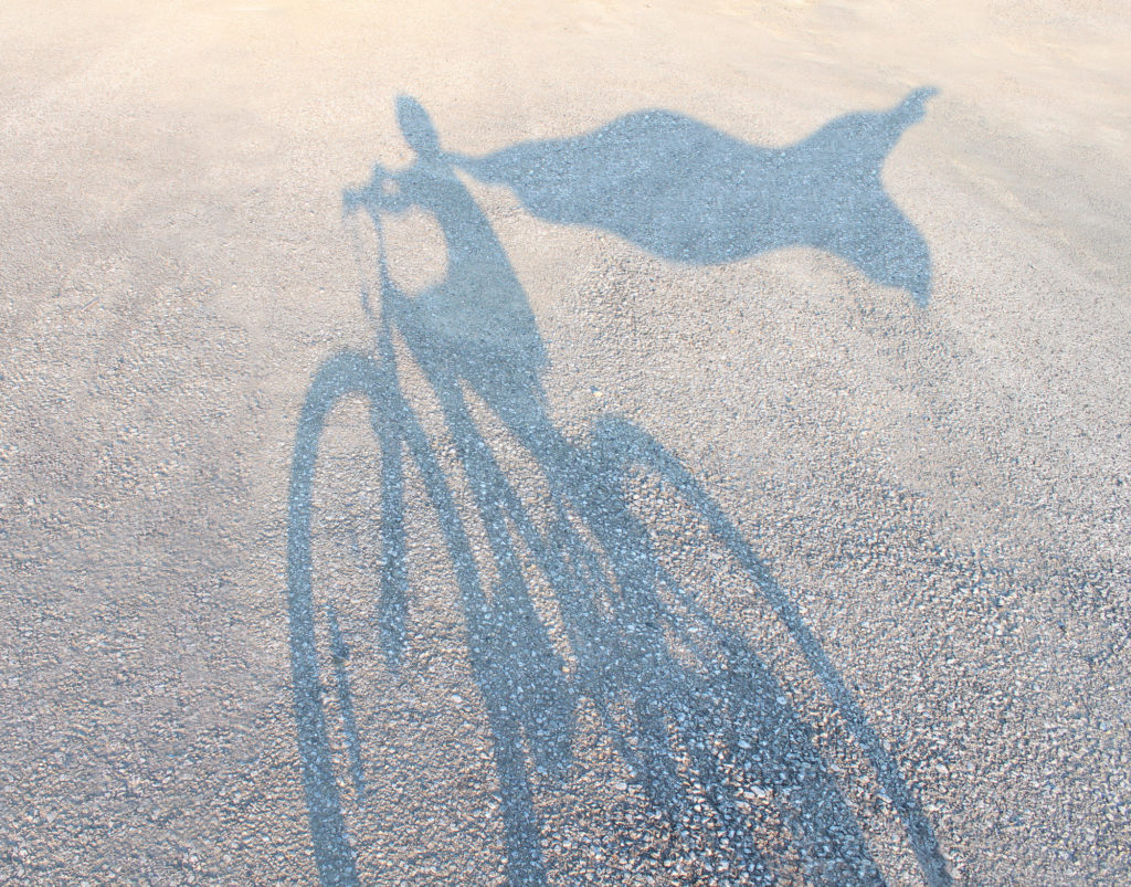 Superhero child wearing a cape riding a bicycle as a cast shadow on a